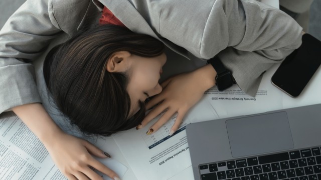 書類の上に突っ伏して休む、忙しそうな女性