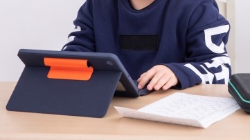 家の机でタブレットを使う子どもの手元