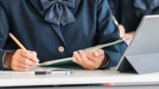 教室で、ノートに書きながらタブレットを使う生徒の手元